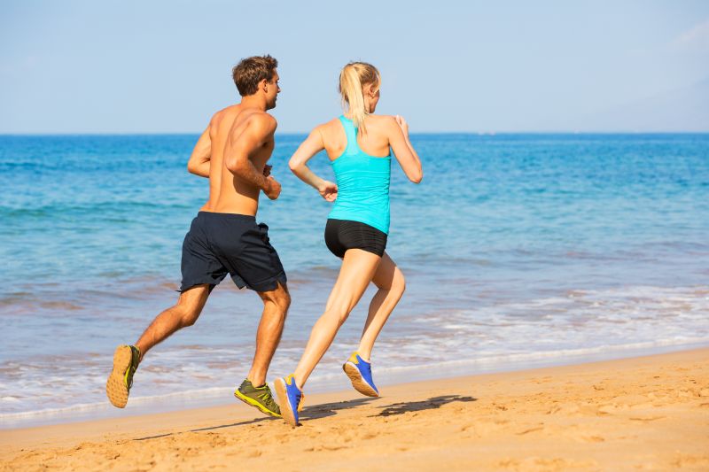 Pareja corriendo.  Corredores deportivos trotando en la playa trabajando sonriendo feliz.  Concepto de ejercicio físico.