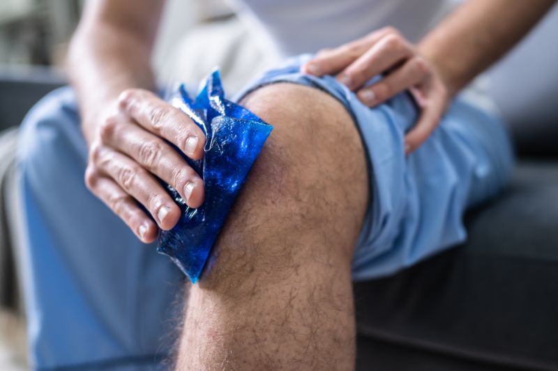 primer plano, de, un, persona que sienta, y, aplicar, hielo, gel, paquete, en, un, rodilla lesionada