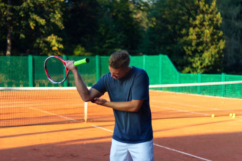 Hombre guapo en la cancha de tenis.  Joven tenista.  Dolor en el codo