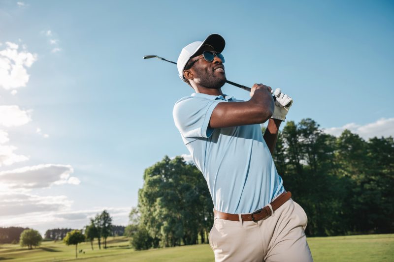 Hombre afroamericano sonriente con gorra y gafas de sol jugando al golf