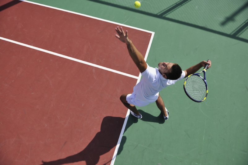 un joven juega tenis al aire libre en un campo de tenis naranja a primera hora de la mañana