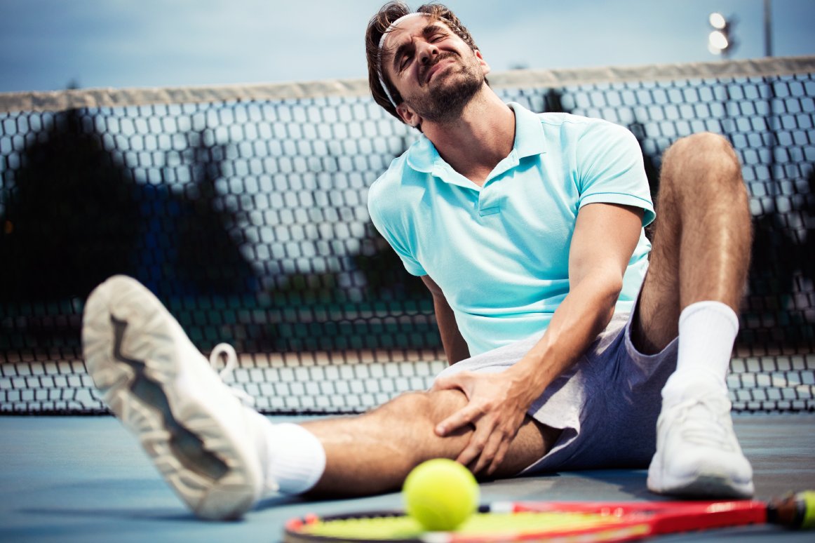 Lesion deportiva.  Joven tenista tocando su rodilla mientras está sentado en la cancha de tenis